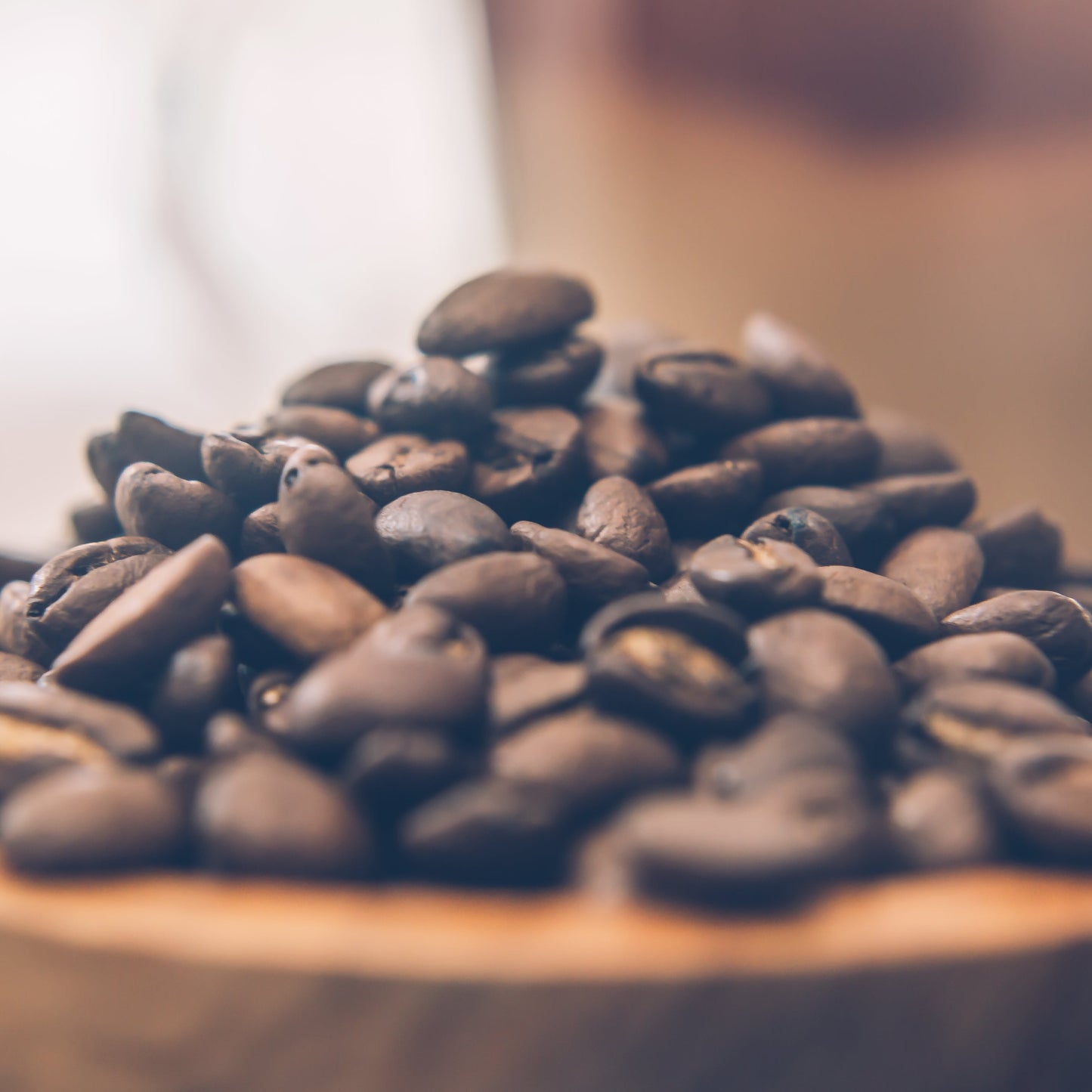 Wooden bowl filled with coffee beans on a blurred background